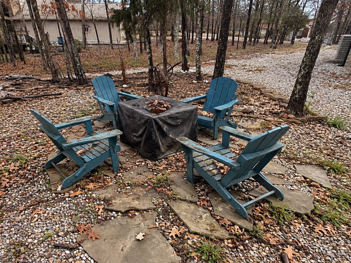 Before β Adirondack chairs and a fire table on loose flagstones in leaf-covered gravel